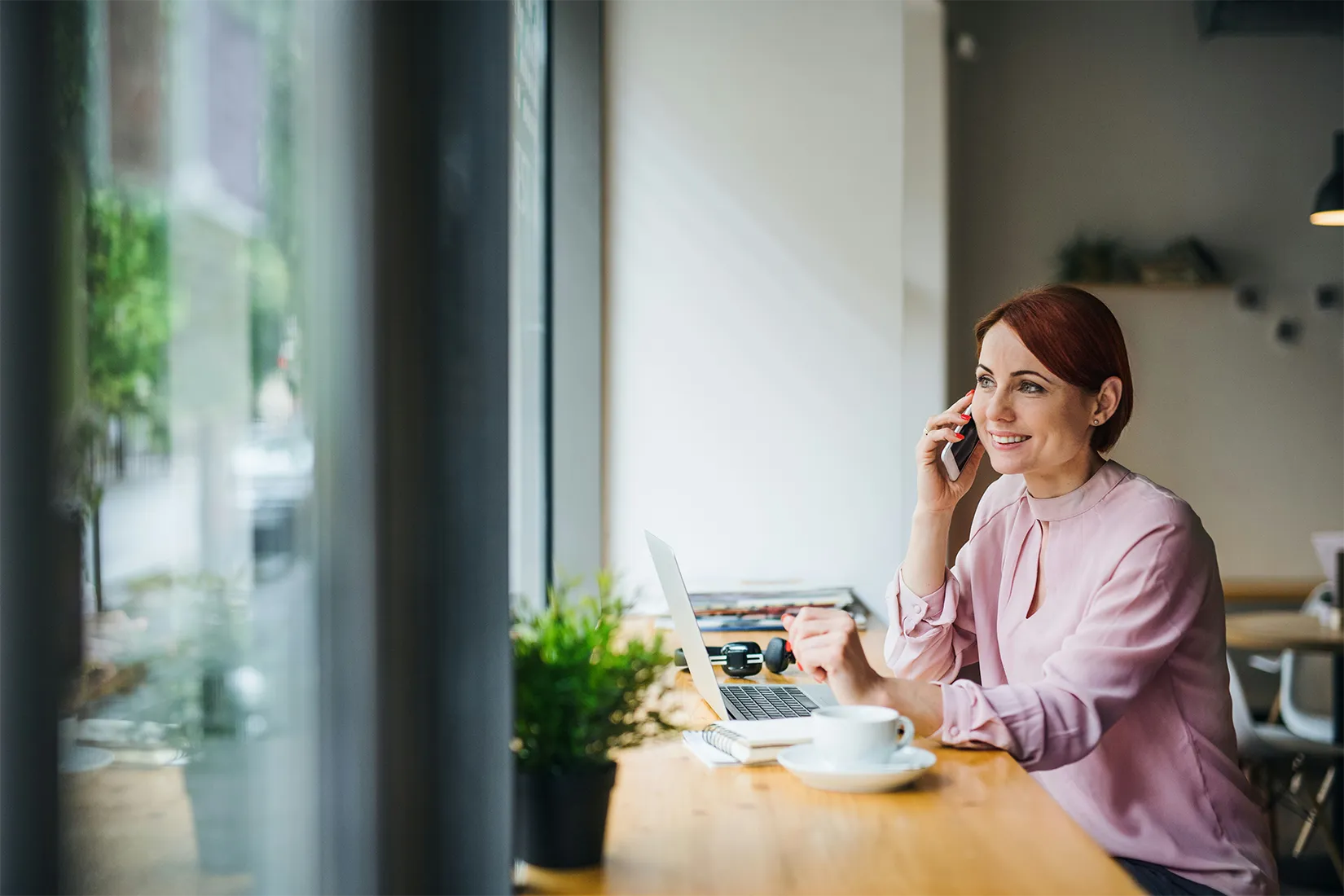 Attraktive Frau mit Kaffee und Telefon sitzt am Tisch in einem Café und telefoniert