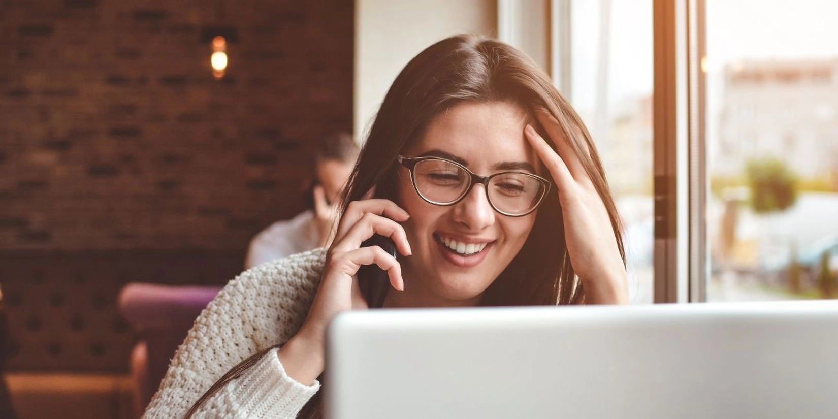 Frau telefoniert mit Smartphone am Laptop sitzend