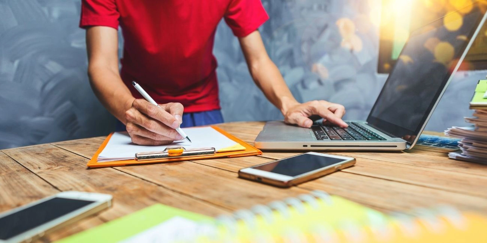 Mann tippt auf Laptop und schreibt auf Papier