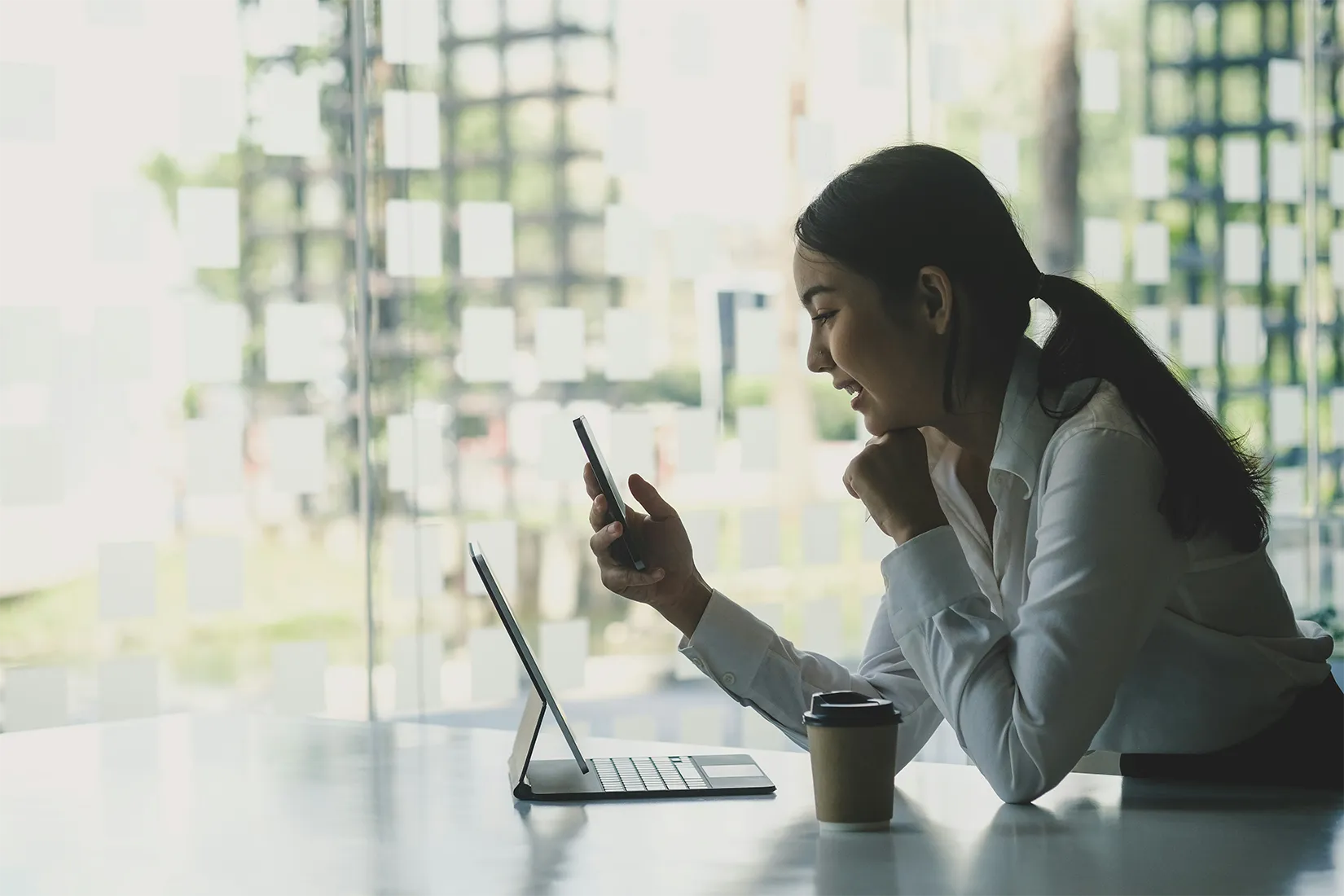 Geschäftsfrau sitzt vor Laptop und telefoniert mit Handy