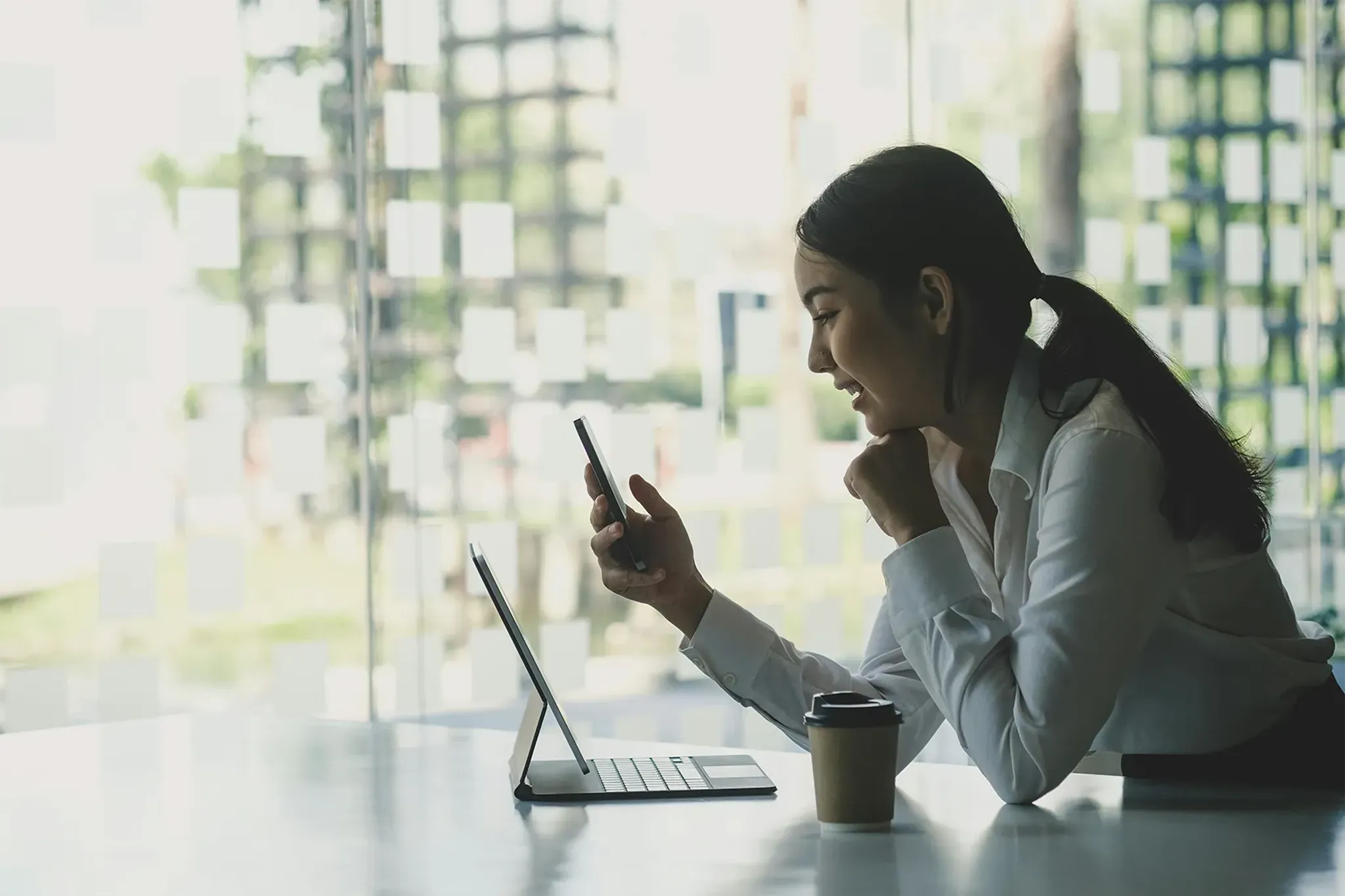 Geschäftsfrau sitzt vor Laptop und telefoniert mit Handy