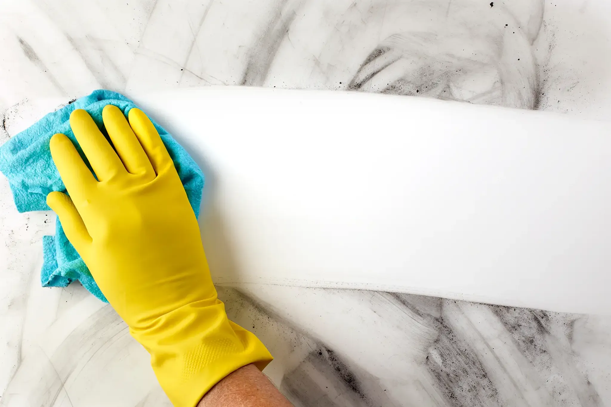 Hand mit gelben Putzhandschuh wischt mit blauem Tuch über schmutzige Oberfläche