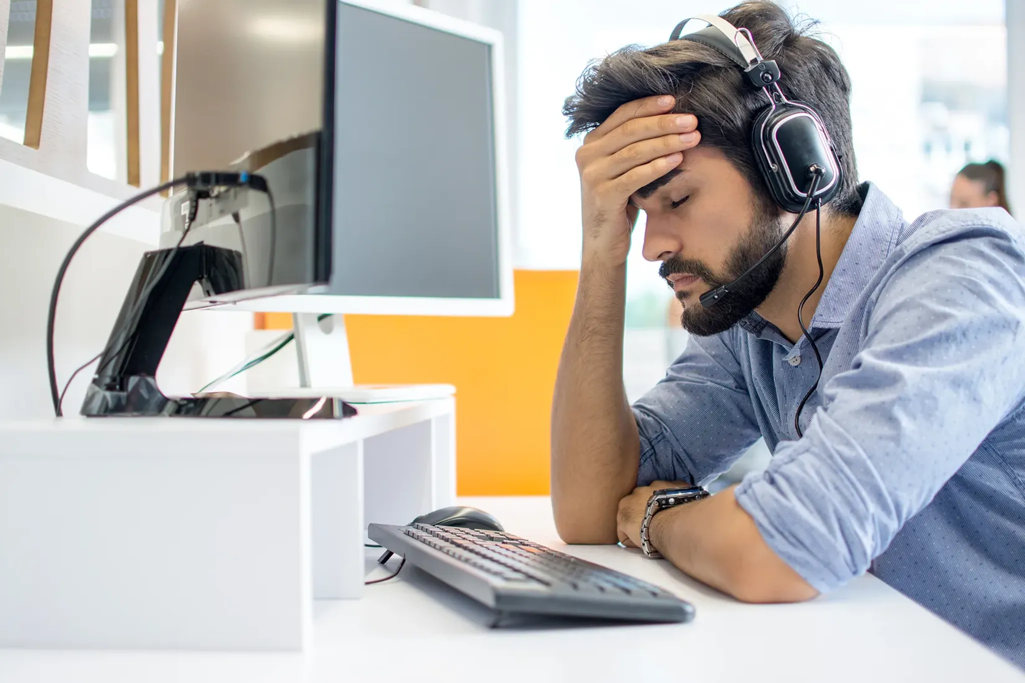 Callcenter Mitarbeiter stützt erschöpft Kopf in die Hände