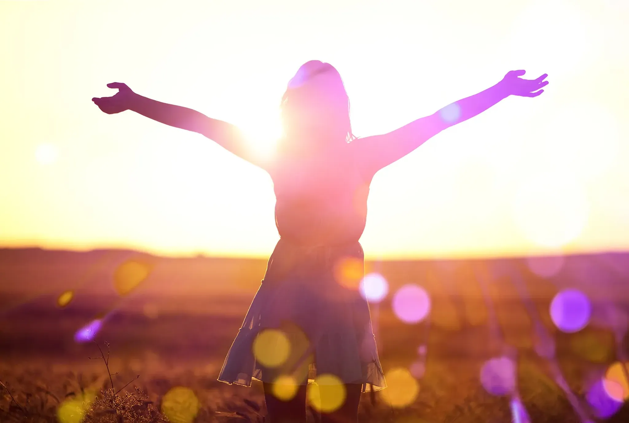 Frau breitet Arme auf sonniger Wiese aus