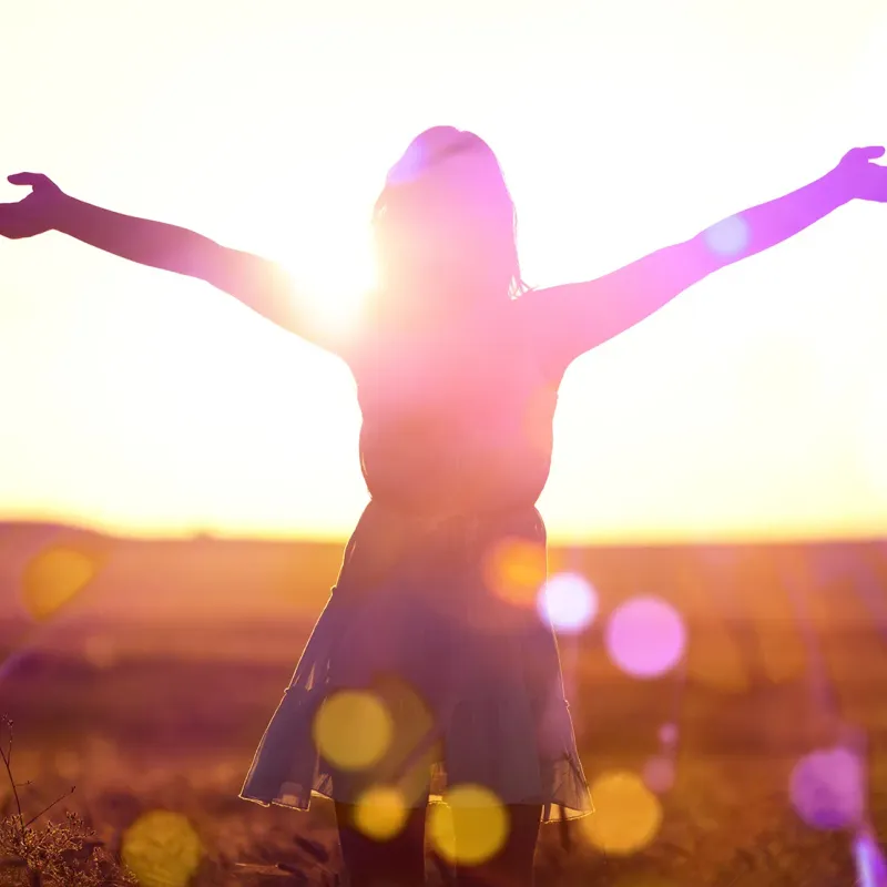 Frau breitet Arme auf sonniger Wiese aus