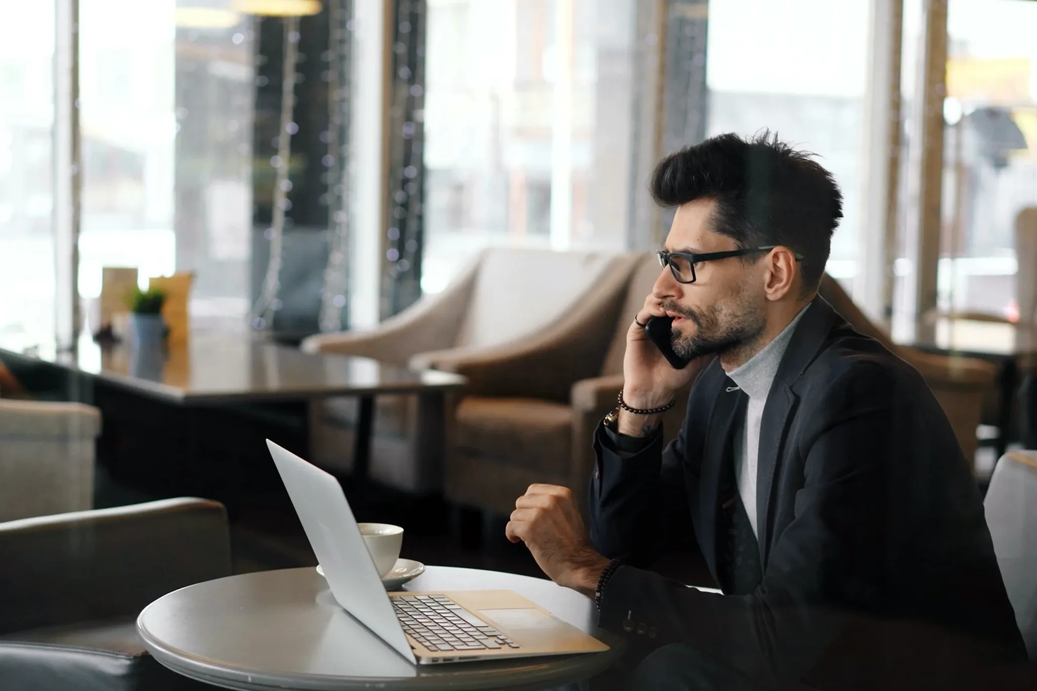 Mann arbeitet mit Laptop in Cafè und telefoniert mit Handy