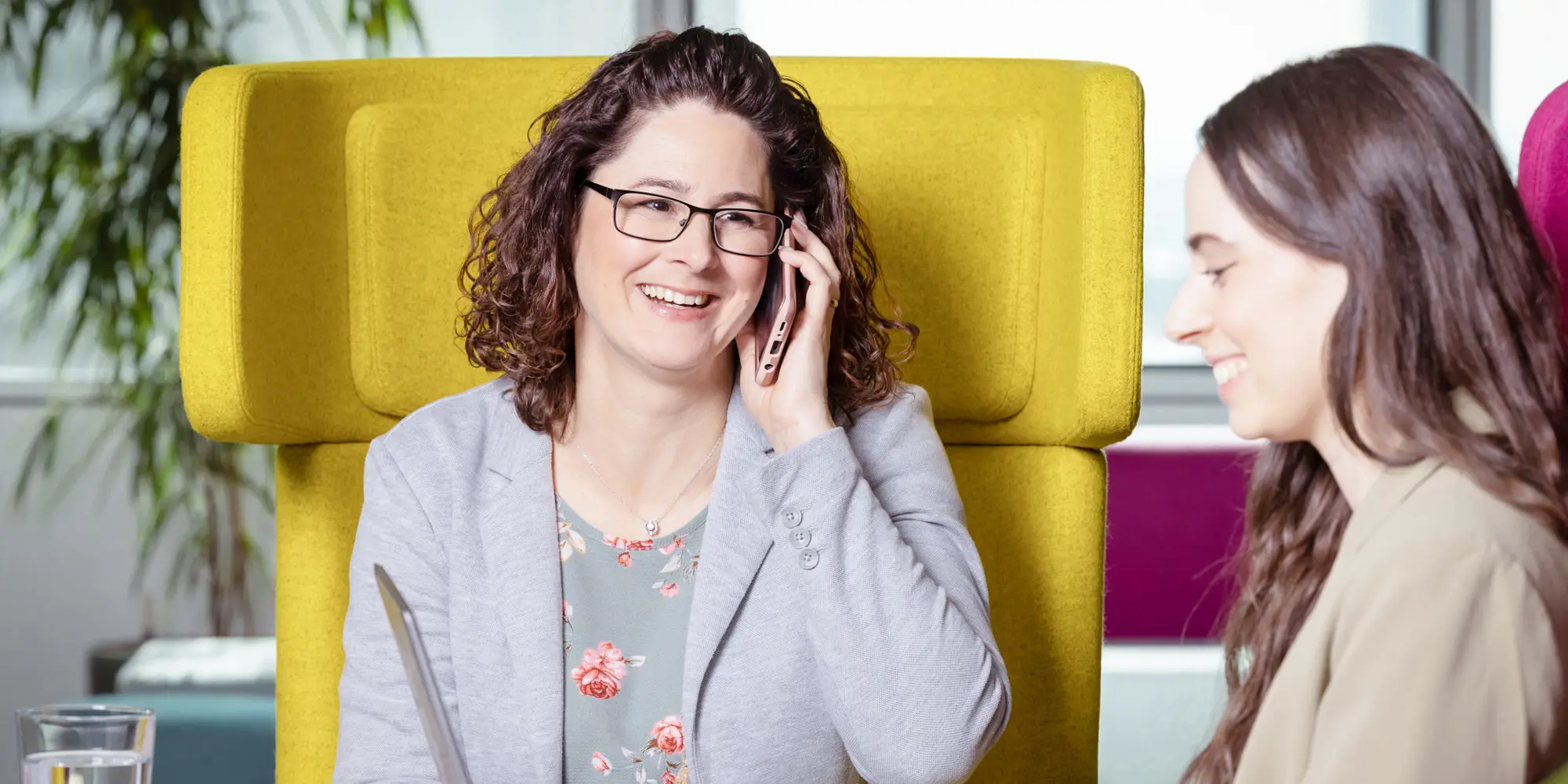 Lachende Frau sitzt in knallgelbem Ohrensessel und telefoniert mit Handy 