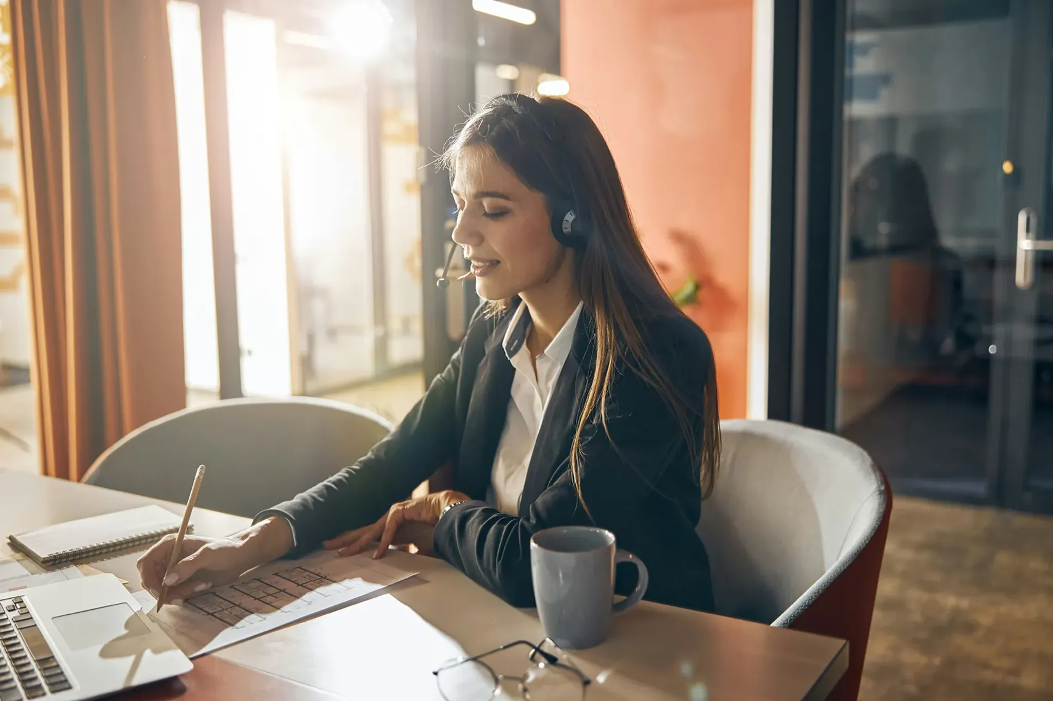 Geschäftsfrau sitzt am Schreibtisch und telefoniert mit Headset