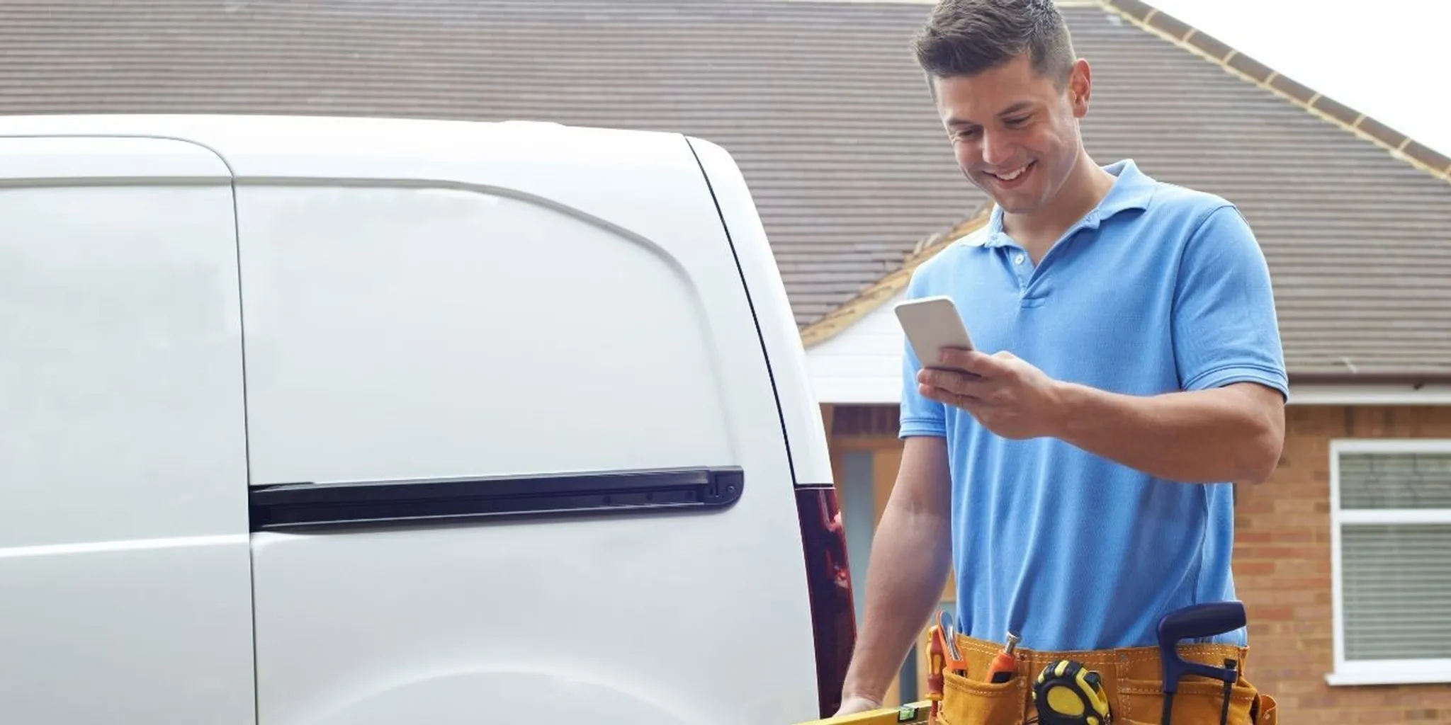 Mann mit Blick auf Handy vor Lieferwagen