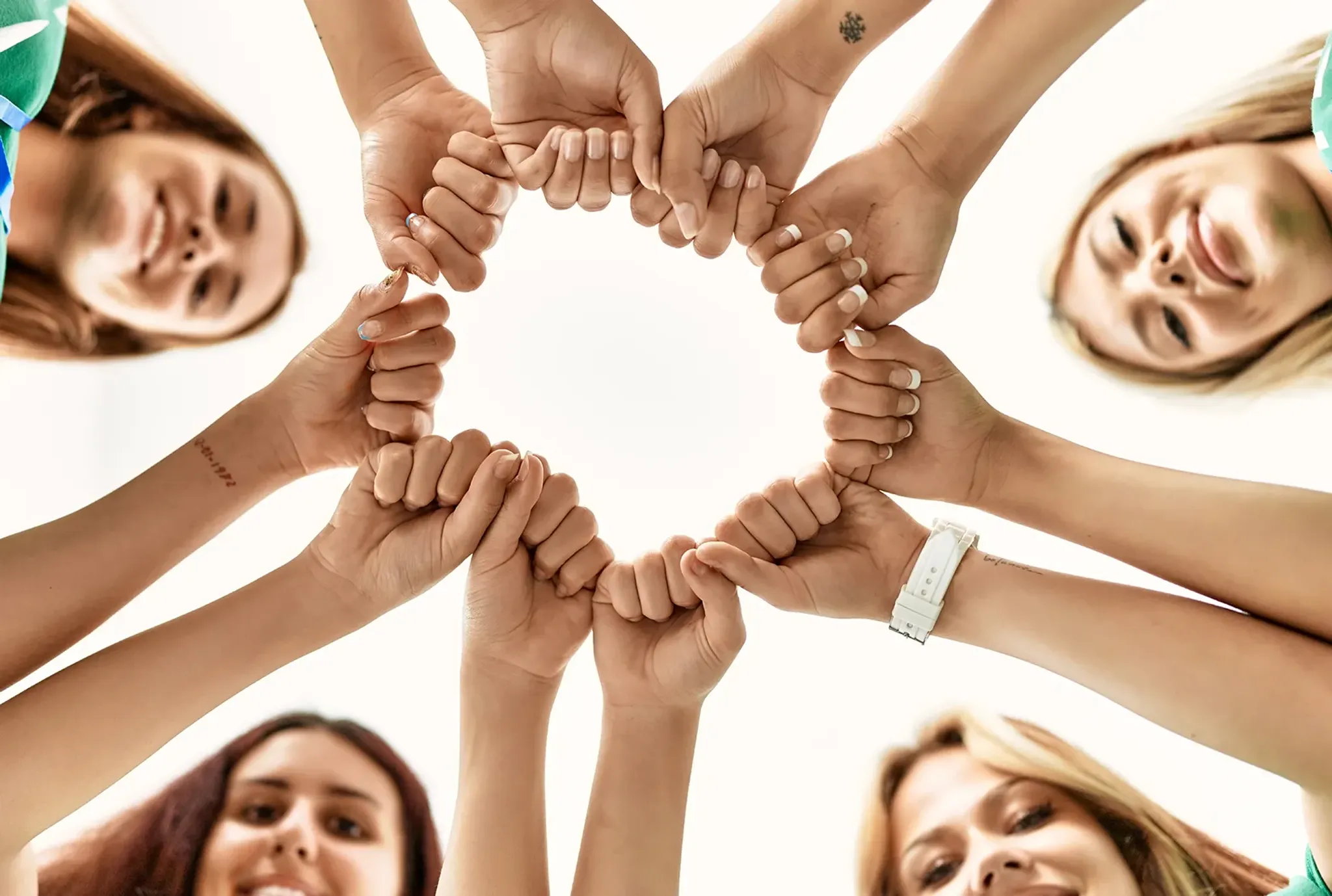 Team an Frauen steht im Kreis und streckt Fäuste zusammen
